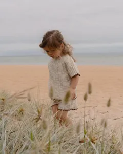 Détail ensemble pull tricot bébé, haut manches courtes bord contrasté et short sur plage.