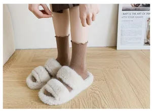 Close-up view of cozy brown ribbed ruffle socks paired with fluffy white slippers on floor.