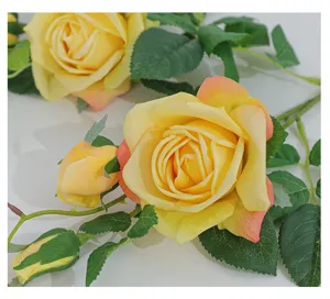 Close-up detail of artificial yellow rose flower head with green leaves for home decor display.