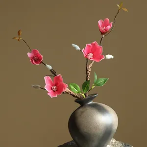 Close-up detail of artificial magnolia flower branch inside dark ceramic vase decor.