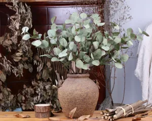 Detailed view of artificial eucalyptus branches in rustic ceramic vase, natural home decor.