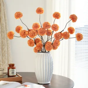 Artificial orange ball chrysanthemum flowers in white ceramic vase for home decor setup.