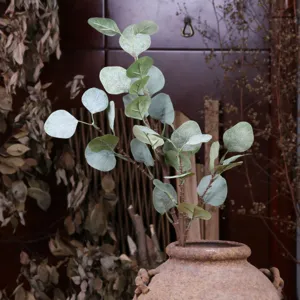 Close-up of artificial eucalyptus branch with frosted leaves in rustic ceramic pot for home decor.