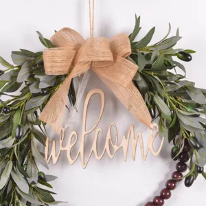 Detailed view of artificial olive leaf wreath with burlap bow and wooden welcome sign decor.