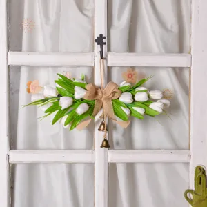 Detailed view of artificial tulip wreath door hanging with green leaves, burlap bow and brass bells.