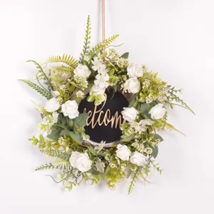 Close-up detail of artificial white rose wreath with green leaves and welcome sign decor.