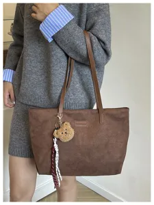 Detailed view of brown suede tote bag with cute bear charm and shoulder strap for commute.
