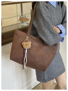 Brown suede tote bag detail view, large capacity shoulder bag with cute bear charm and ribbon.