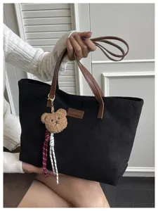 Detailed view of the black tote bag featuring brown handles, chic bear pendant and label.