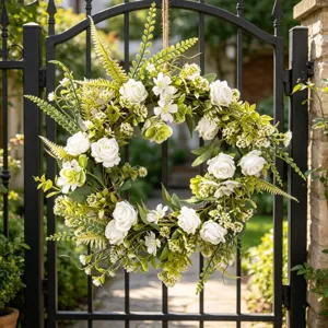 Close-up detail of the artificial white rose and green foliage wreath hanging outdoors.