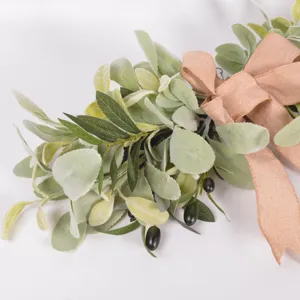 Primer plano detallado de guirlanda con ramas de olivo artificiales y lazo rústico de yute.