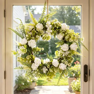 Artificial white rose wreath detail showing lush green leaves and vine base on glass door.
