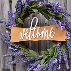 Detailed close-up of a purple lavender floral wreath with a wooden welcome sign on wall.