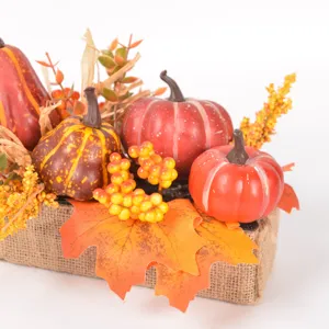 Closeup of artificial autumn pumpkins, colorful maple leaves, and berries in burlap planter.