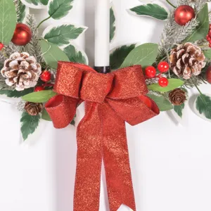 Détail de la couronne de Noël avec pommes de pin givrées, baies rouges et nœud rouge brillant.