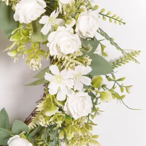 Detailed close-up of artificial white rose wreath with green leaves, elegant floral decor.