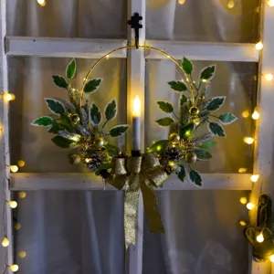 Detail de couronne de Noel avec feuilles vertes, pommes de pin, noeud dore et bougie.