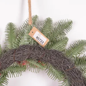 Close-up detail of artificial pine needle Christmas wreath with hanging tag and rustic vine base.