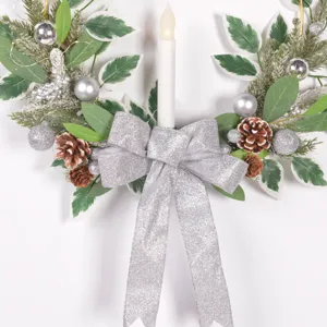Détail de couronne de bougie de Noël avec nœud argenté, pommes de pin et feuilles artificielles.