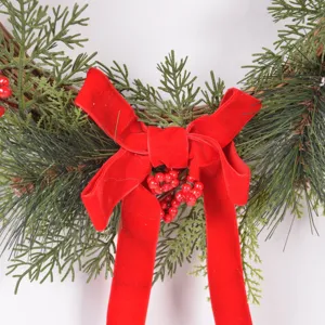 Christmas wreath detail shot featuring realistic pine branches, red berries and velvet bow.