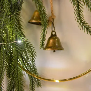 Christmas Norfolk pine wreath wall hanging with brass bells and fairy lights for home decor.