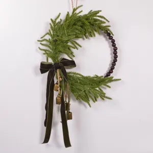 Norfolk pine Christmas wreath with wooden beads, velvet bow, and brass bells for holiday decor.