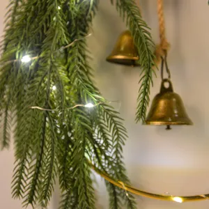Christmas Norfolk pine wreath hanging with bells and LED lights for holiday home wall decor