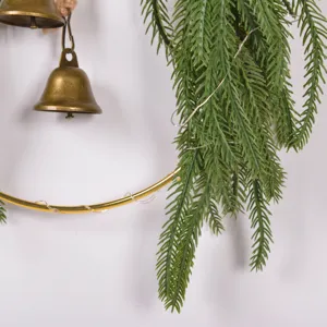 Close-up detail of artificial Norfolk pine branch, brass bell and metal hoop decor.