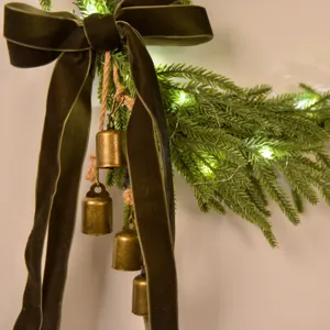 Christmas Norfolk pine wreath decoration with dark green velvet bow and rustic brass bells.