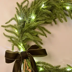 Artificial Norfolk pine Christmas wreath with velvet bow and warm fairy lights for holiday decor.