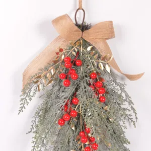 Christmas artificial pine branch teardrop swag detail with red berries gold leaves burlap bow.