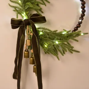 Christmas wreath detail featuring Norfolk pine, velvet bow, bells, and warm LED string lights.