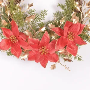 Ghirlanda natalizia decorativa con poinsettia rosse, foglie dorate e aghi di pino verdi.