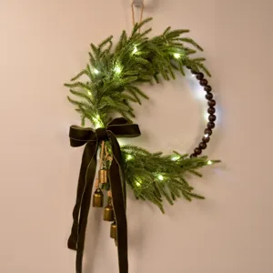 Christmas Norfolk pine wreath with wooden beads, velvet bow, fairy lights for decor.