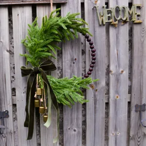 Christmas Norfolk pine wreath detail view, featuring dark green velvet bow and wood beads.