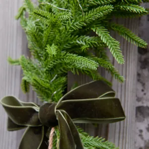 Artificial Norfolk pine Christmas decorative branch with velvet bow wall hanging detail.
