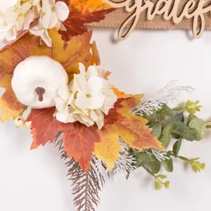 Close-up of autumn artificial maple leaves, white pumpkin, and grateful wooden sign detail.