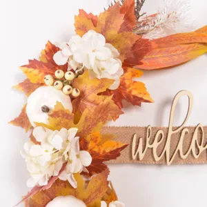 Autumn wreath detail showing artificial maple leaves, white pumpkin and welcome sign.