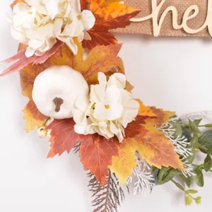 Close-up of autumn wreath detail featuring artificial maple leaves and white pumpkin.