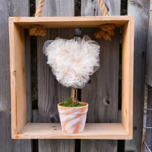 Close-up of a romantic heart-shaped tulle tree potted ornament, rustic wood box background.