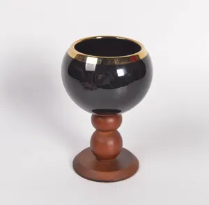 Primo piano dettagliato della tazza in ceramica nera con bordo dorato e base in legno.