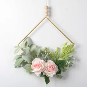 Detail view of geometric metal hanging wall decor with artificial pink roses and green leaves.