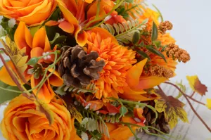 Autumn artificial flower bouquet detail shot, featuring orange roses, pine cones and autumn leaves.