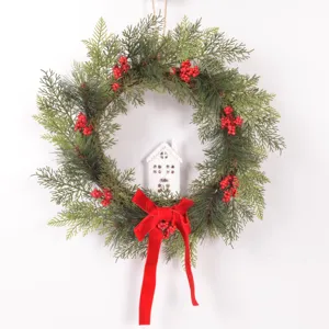 Christmas wreath with pine branches, red berries, white house ornament and red velvet bow.