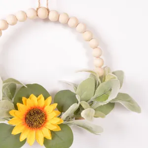Wooden bead wreath with faux sunflower and green leaves for seasonal home wall decor.