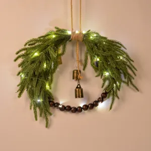 Norfolk pine Christmas wreath detail with wooden beads, brass bells, and LED lights for wall hanging.