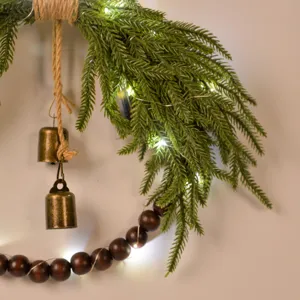Close-up detail of artificial Norfolk pine Christmas wreath with wooden beads and bronze bells.