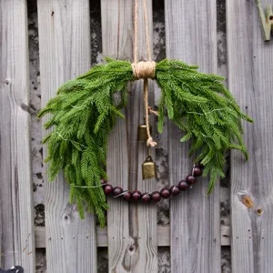 Close up of Christmas decorative wreath with Norfolk pine branches, wood beads and bells.