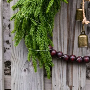Christmas Norfolk pine wreath detail with wood beads and rustic brass bells hanging decor