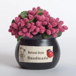 Close-up of a mini potted artificial pink berry plant with a black ceramic pot and fabric label.